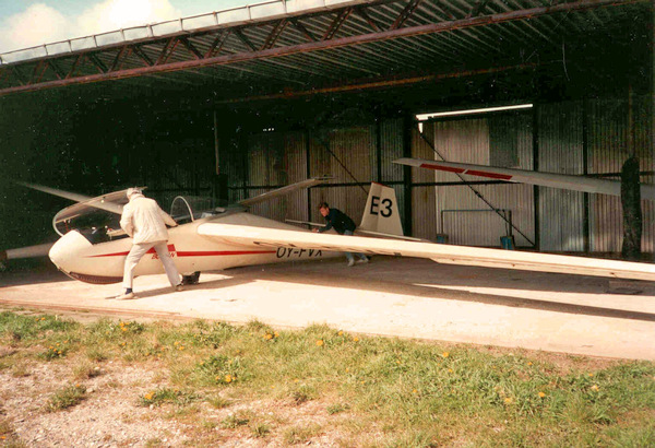 Henning Yde + ukendt i færd med at manøvrere Bocian OY-FVX (E3) ud af blikhangaren.